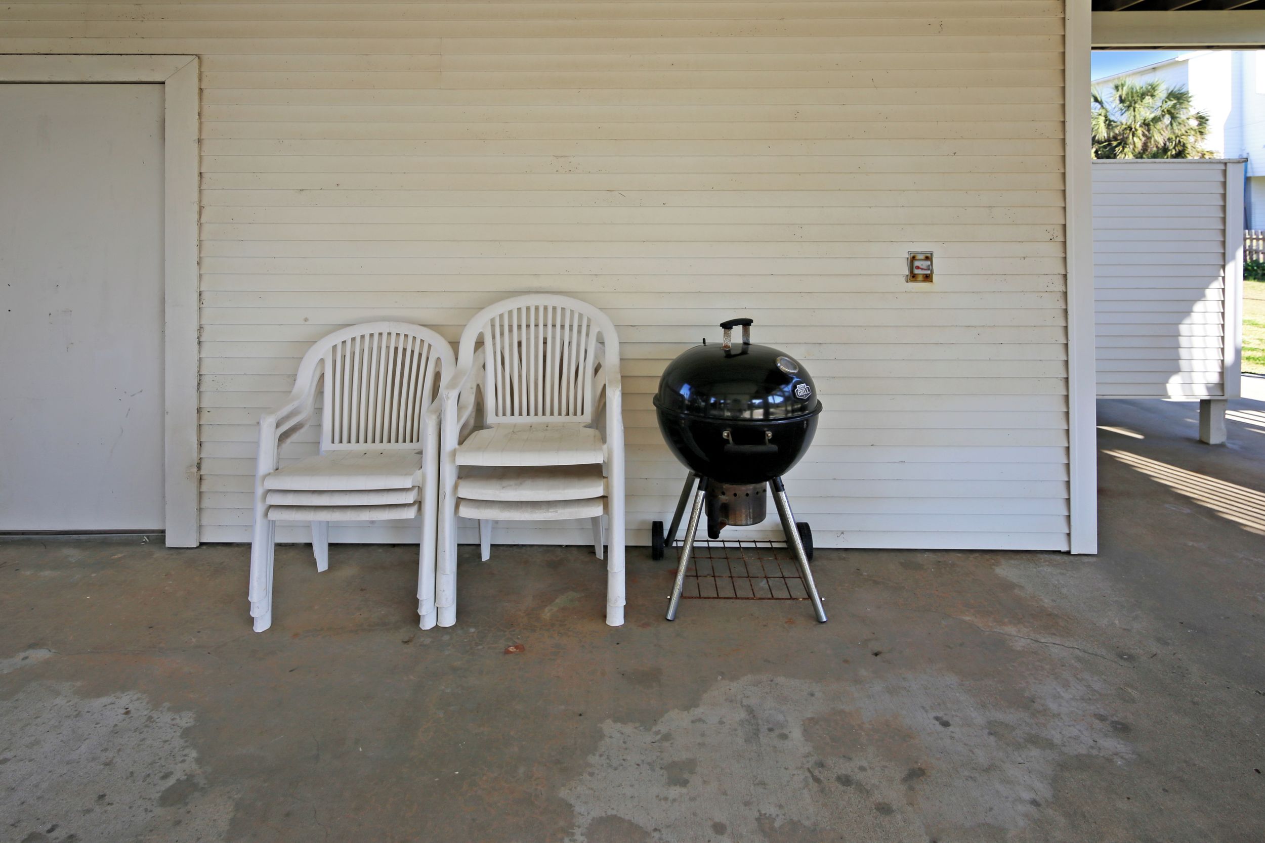Un garage avec deux chaises en plastique blanches et un barbecue noir.
