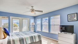 A bedroom with a bed, a ceiling fan, a dresser, a TV, and a window with blinds.