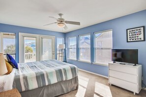 Une chambre à coucher comprenant un lit, un ventilateur de plafond, une commode, un téléviseur et une fenêtre avec des stores.