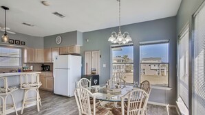 A modern kitchen with a dining area, featuring a large window, white cabinetry, and a glass dining table. - Mutiny on the Bounty by Ryson Vacation Rentals (Galveston)