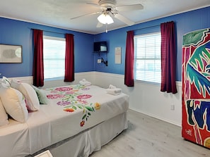 A bedroom with a bed, a ceiling fan, a TV, and a window with curtains. - Paradise Found by Ryson Vacation Rentals (Galveston)