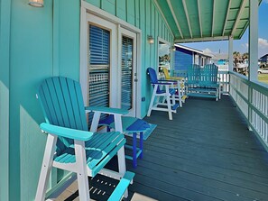A covered porch with turquoise Adirondack chairs and a wooden deck.