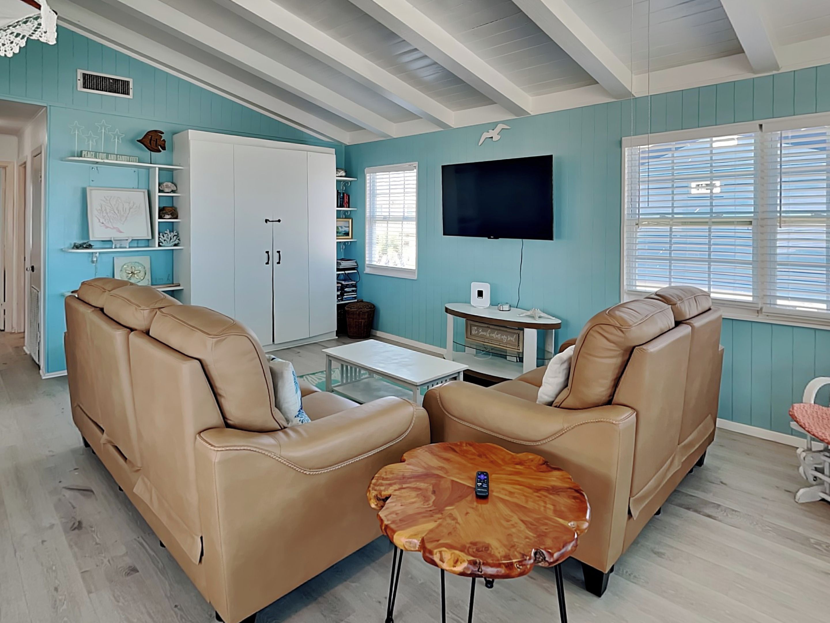 A living room with two beige leather sofas, a wooden coffee table, a flat-screen TV, and a bookshelf with decorative items.