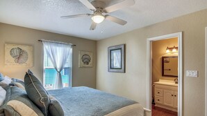 A bedroom with a bed, a ceiling fan, and a bathroom visible through an open door. - Pirates' Treasure by Ryson Vacation Rentals (Galveston)