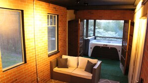 Une pièce chaleureuse avec un mur en briques, une fenêtre, un canapé et une vue sur un jacuzzi situé à l’extérieur.