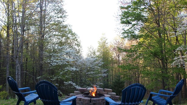 Un feu de camp entouré de quatre chaises bleues, le tout situé dans un cadre forestier.