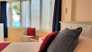 Habitación de hotel con cama, una mesita, una silla y vistas al océano a través de amplias ventanas.
