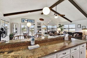 A spacious kitchen with a granite countertop, wooden beams, and large windows offering views of the outdoors. - Prager Bay View by Ryson Vacation Rentals (Galveston)
