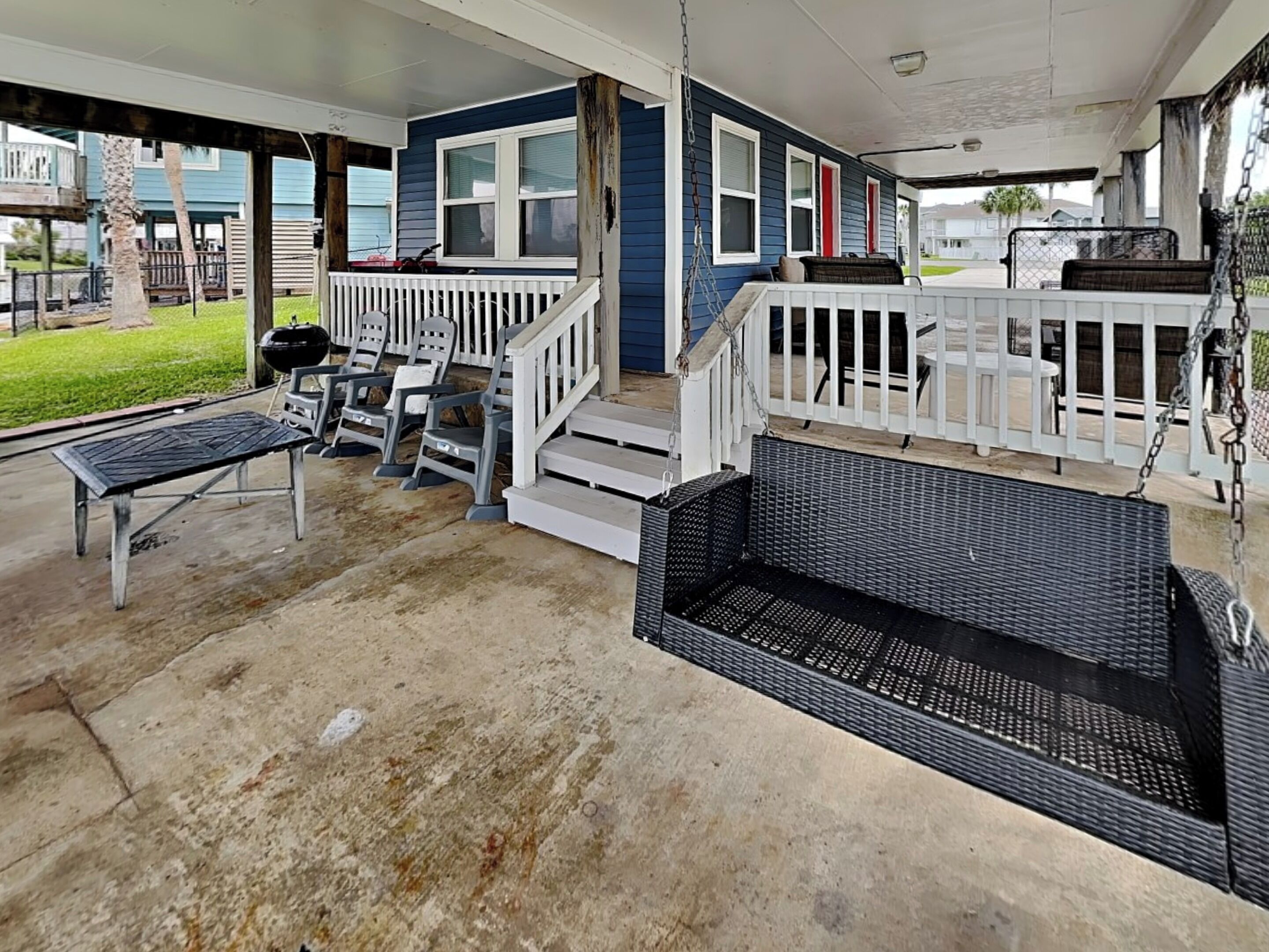 A covered porch with a swing seat, a grill, and a dining area with outdoor furniture.
