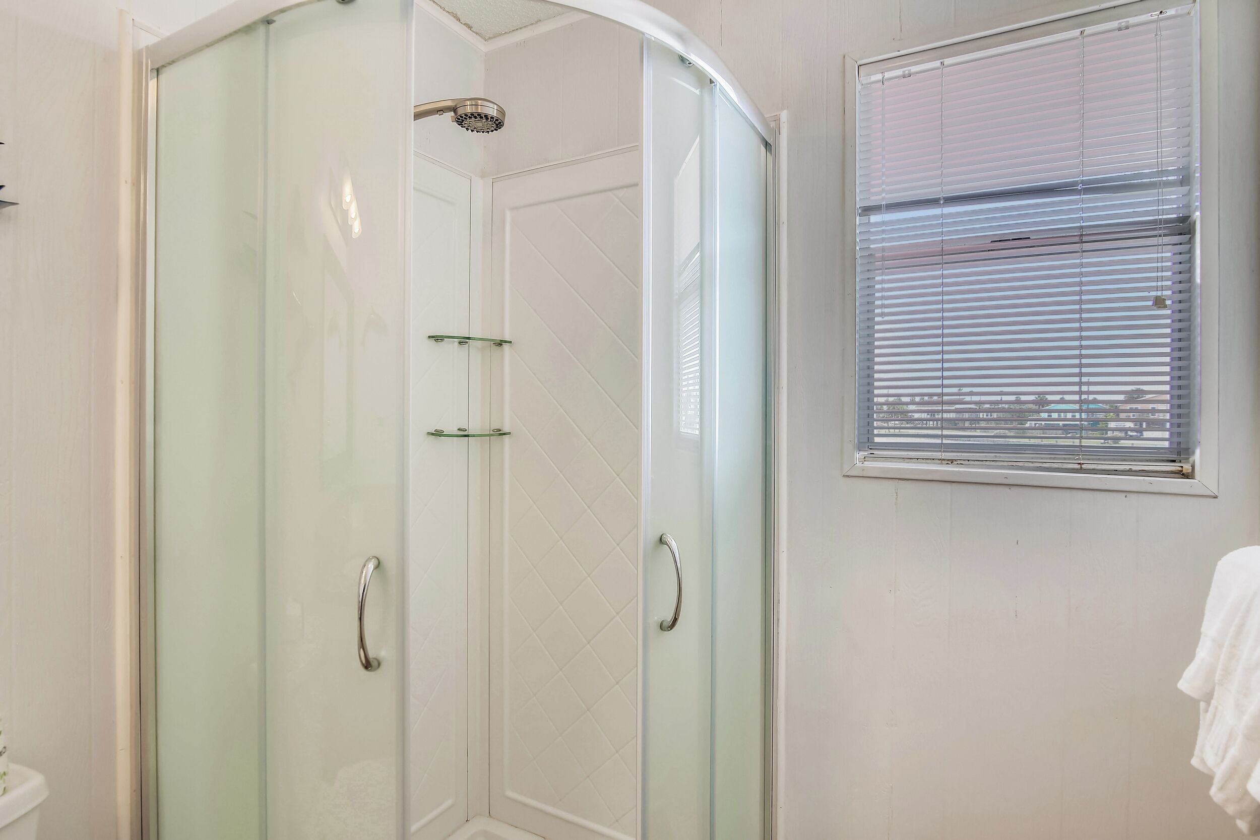 A glass-enclosed shower with a handheld showerhead, a glass door, and a window with blinds.