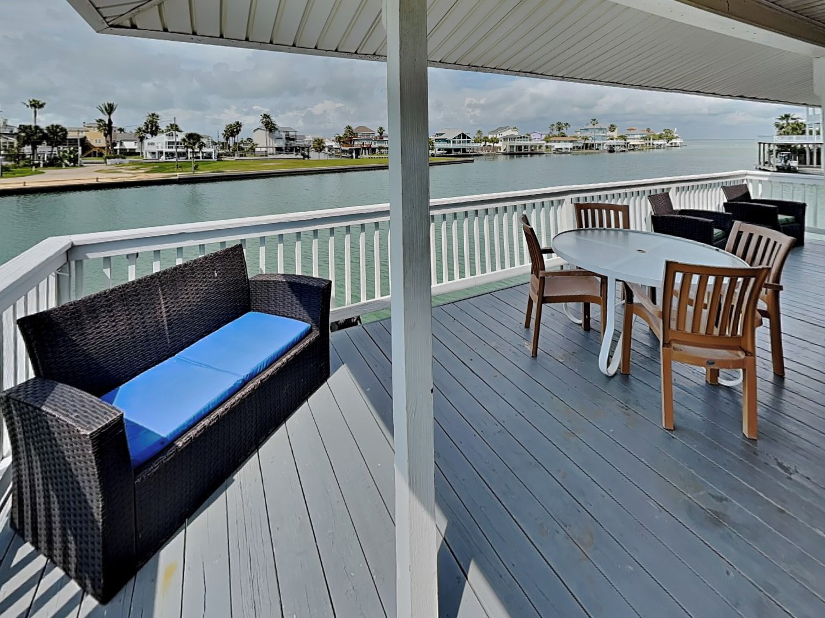 A covered outdoor deck with a sofa and table, overlooking a body of water and a marina.