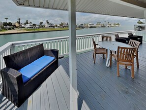 A covered outdoor deck with a sofa and table, overlooking a body of water and a marina.