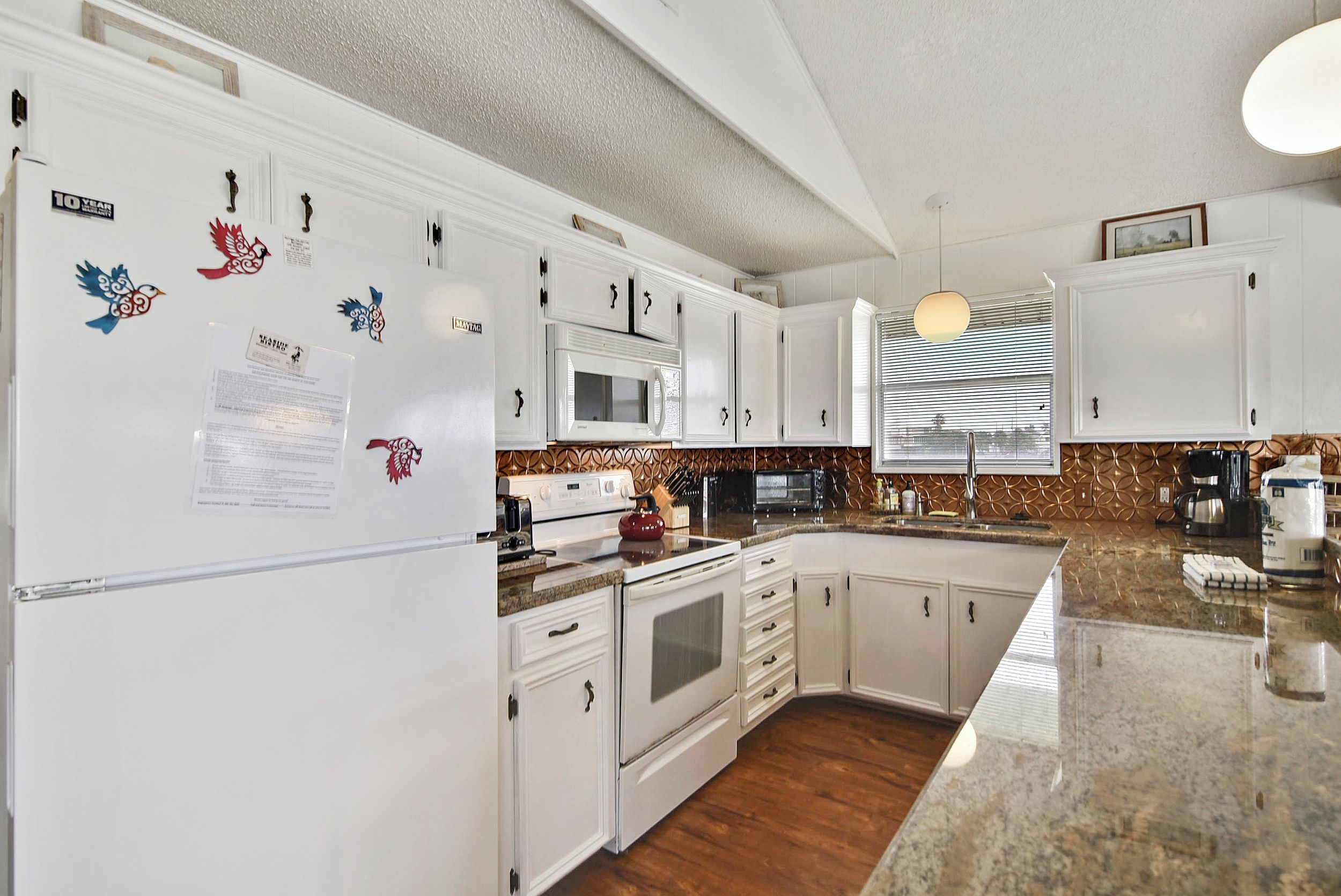 A modern kitchen with white cabinetry, a granite countertop, a built-in microwave, and a stove.
