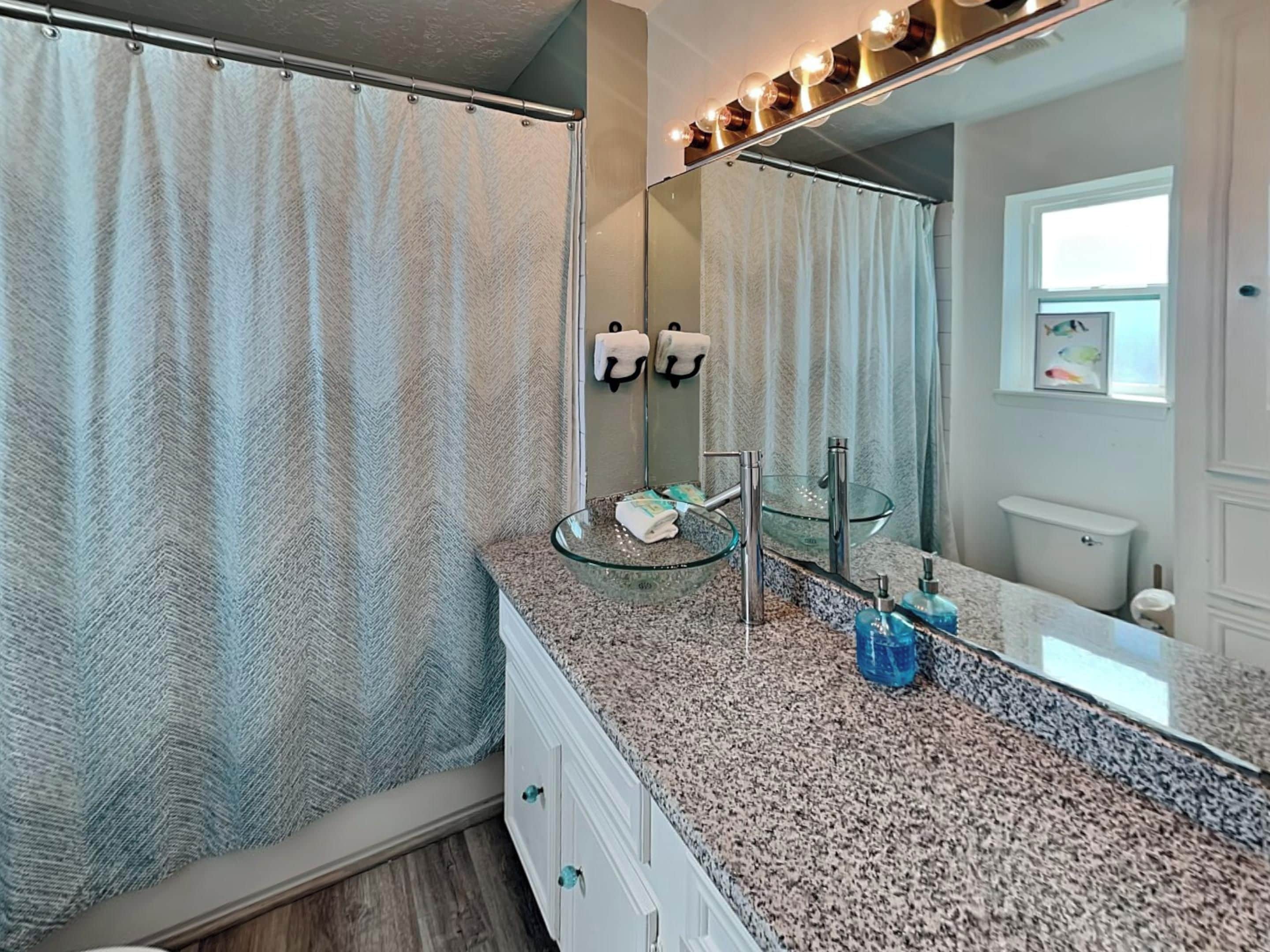 A bathroom with a glass sink, a large mirror, and a shower curtain.