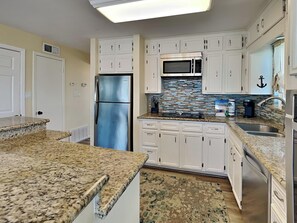 Eine Küche mit weißen Schränken, einem Edelstahlkühlschrank, einer Mikrowelle, Granit Arbeitsplatten und einem gemusterten Teppich.