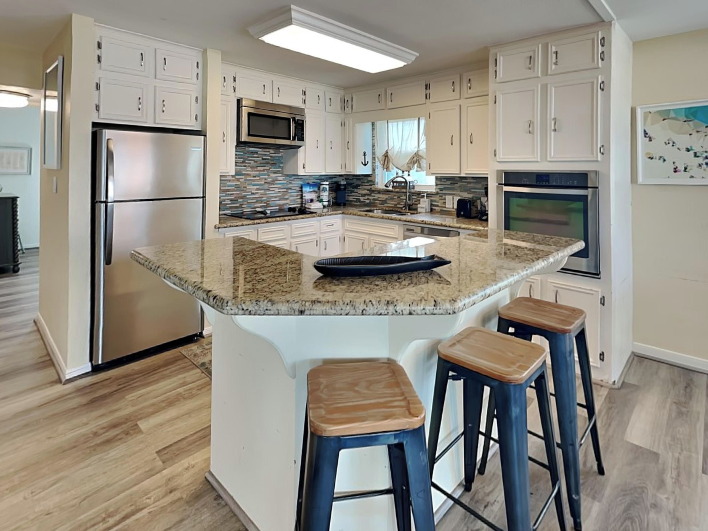 Una cocina moderna con armarios blancos, encimera de granito y refrigerador de acero inoxidable.