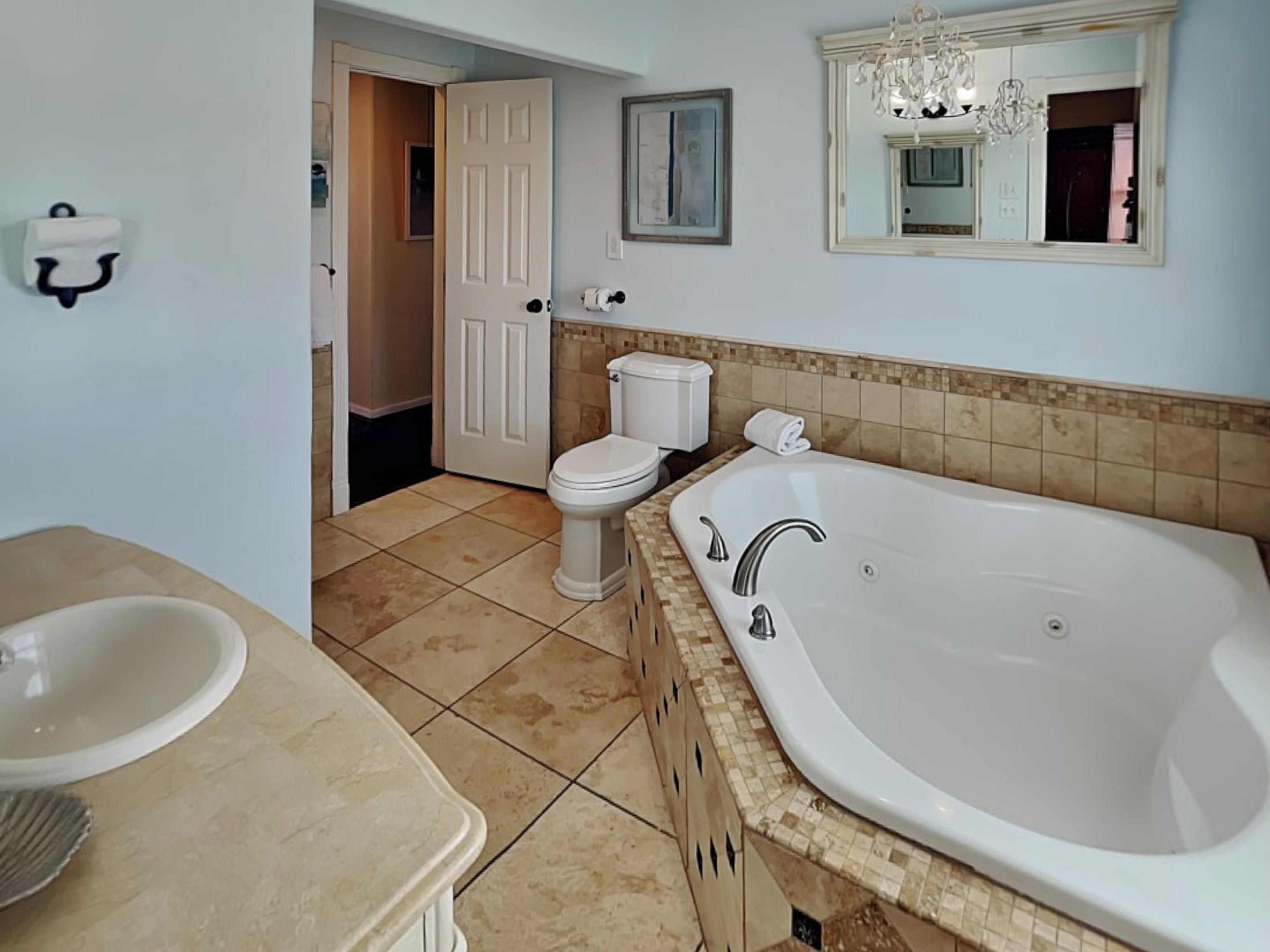 Un baño con bañera, inodoro, lavabo y una puerta que da a otra habitación.