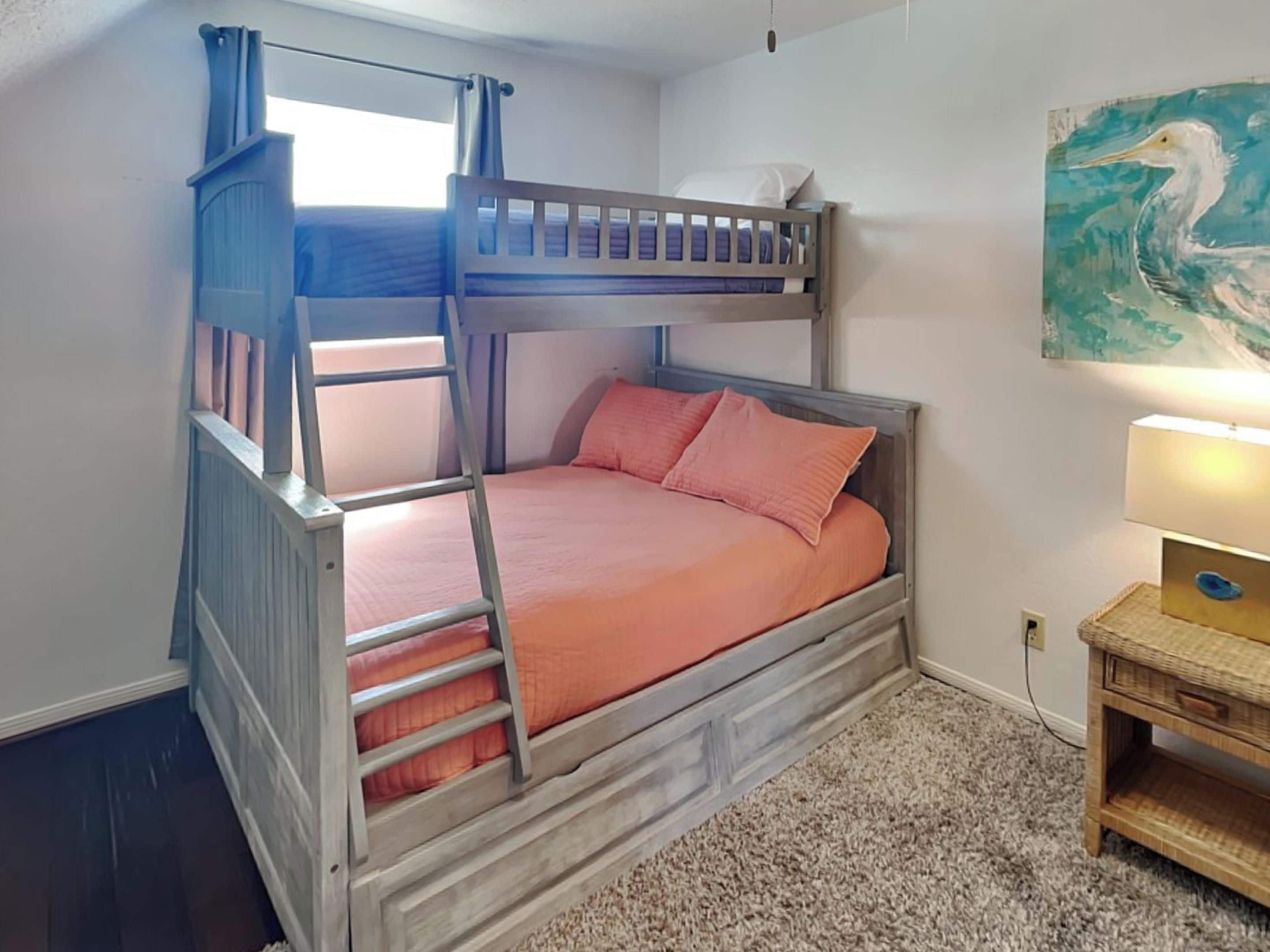 A bunk bed with a ladder, a small bedside table with a lamp, and a painting on the wall.