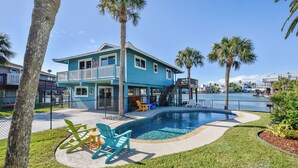 A two-story house with a pool, surrounded by palm trees and a fence. - Reel Paradise by Ryson Vacation Rentals (Galveston)