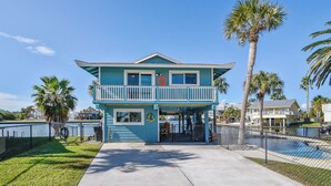 A two-story building with a balcony, a fenced area, and a pool. - Reel Paradise by Ryson Vacation Rentals (Galveston)