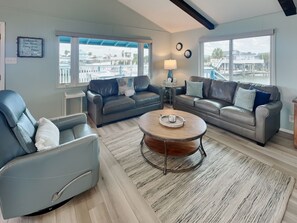 A modern living room with two sofas, a coffee table, and a view of a marina. - Reel Paradise by Ryson Vacation Rentals (Galveston)