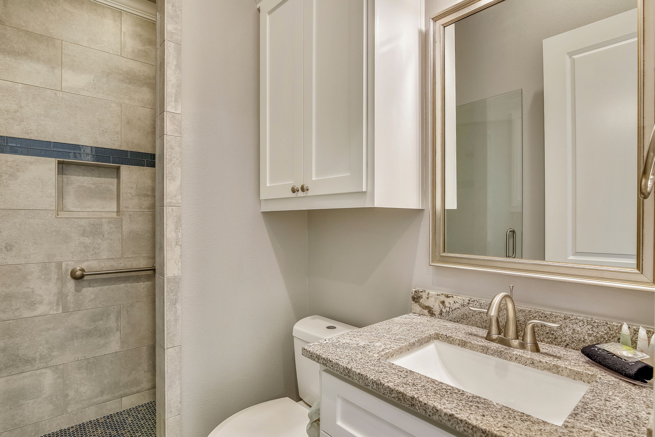 A bathroom with a shower, toilet, sink, and cabinets.