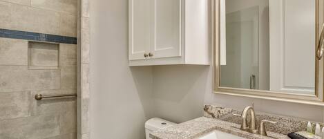 A bathroom with a shower, toilet, sink, and cabinets.