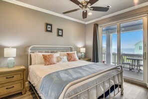 A bedroom with a bed, bedside tables, a ceiling fan, and a view of the outdoors. - Salty Blue Mermaid by Ryson Vacation Rentals (Galveston)