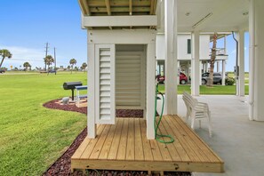 A covered outdoor deck with a wooden table and chairs, a hose, and a grill. - Salty Blue Mermaid by Ryson Vacation Rentals (Galveston)