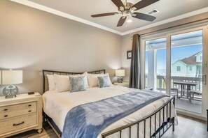 A bedroom with a bed, nightstands, a ceiling fan, and a view of the outside balcony. - Salty Blue Mermaid by Ryson Vacation Rentals (Galveston)