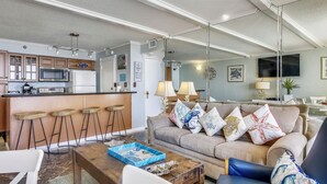 En moderne stue med en grå sofa, et træbord og et køkkenområde med bar og bænke.