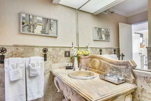 A bathroom with a marble vanity, a large mirror, and two framed pictures on the wall. - Luis' Lair by Ryson Vacation Rentals (Galveston)