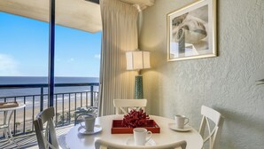 Uma sala de jantar com mesa, cadeiras, abajur, quadro emoldurado e vista para o oceano.