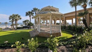 A gazebo with a white railing, surrounded by a well-maintained lawn and flowering plants. - Luis Landing by Ryson Vacation Rentals (Galveston)