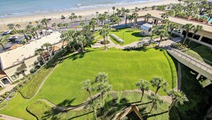 A hotel with a large lawn, palm trees, and a view of the beach. - Luis Landing by Ryson Vacation Rentals (Galveston)