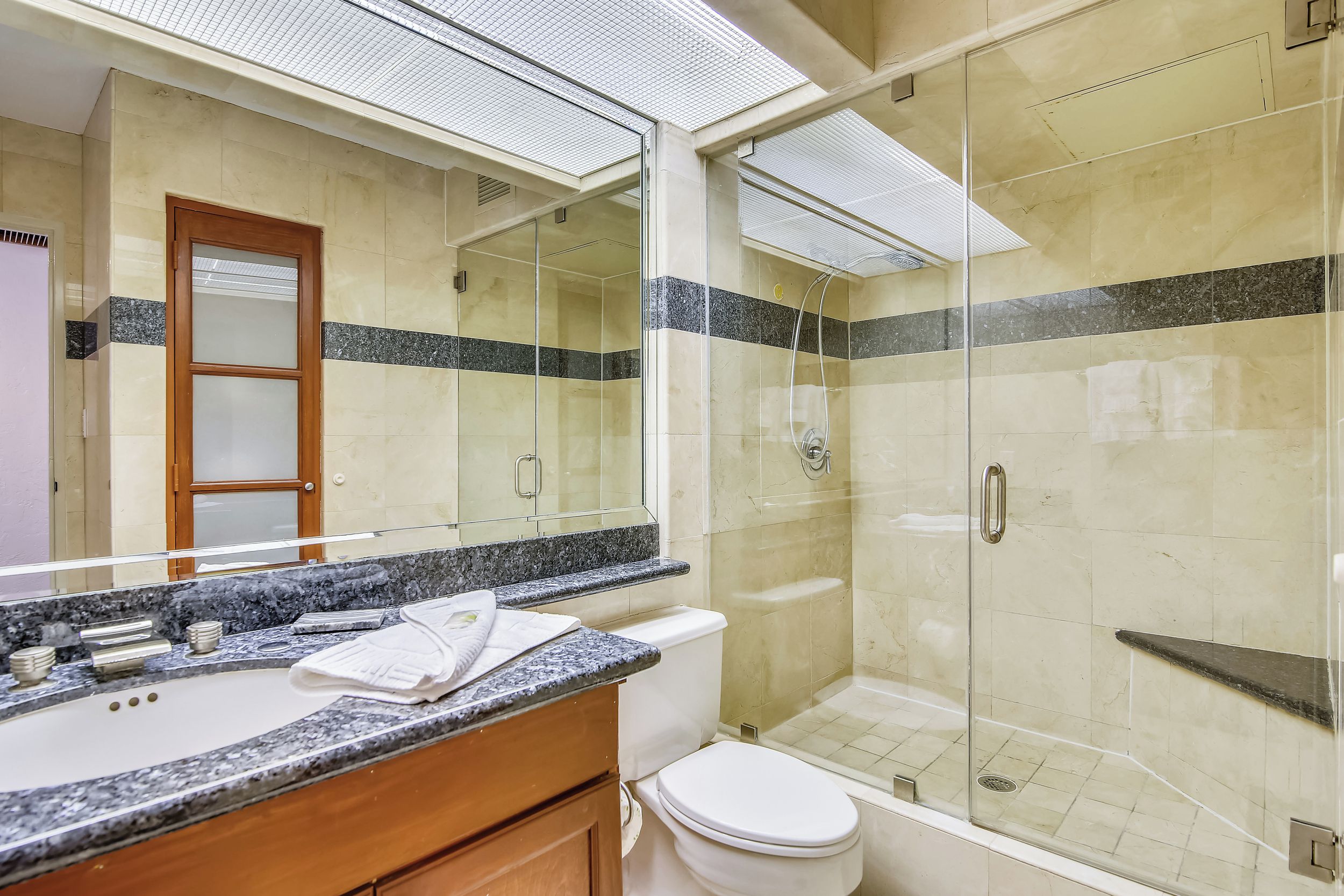 A modern bathroom with a glass-enclosed shower, a large mirror, and a granite countertop.