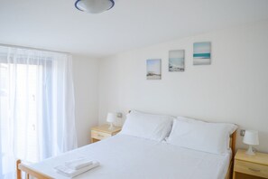 A bedroom with a bed, two bedside tables, a window with sheer curtains, and three wall-mounted pictures. - Green Bay Village - B19 - Two-room apartment (Foggetta)