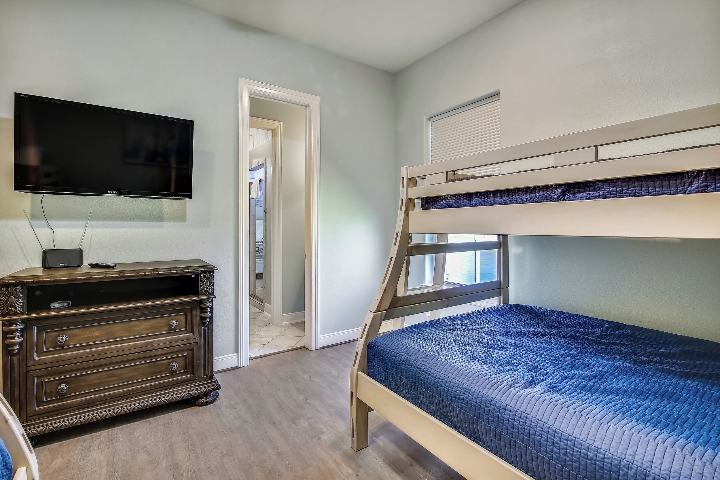 Una habitación con una cama literera, un televisor sobre un mueble de madera y una puerta que da a otra estancia.