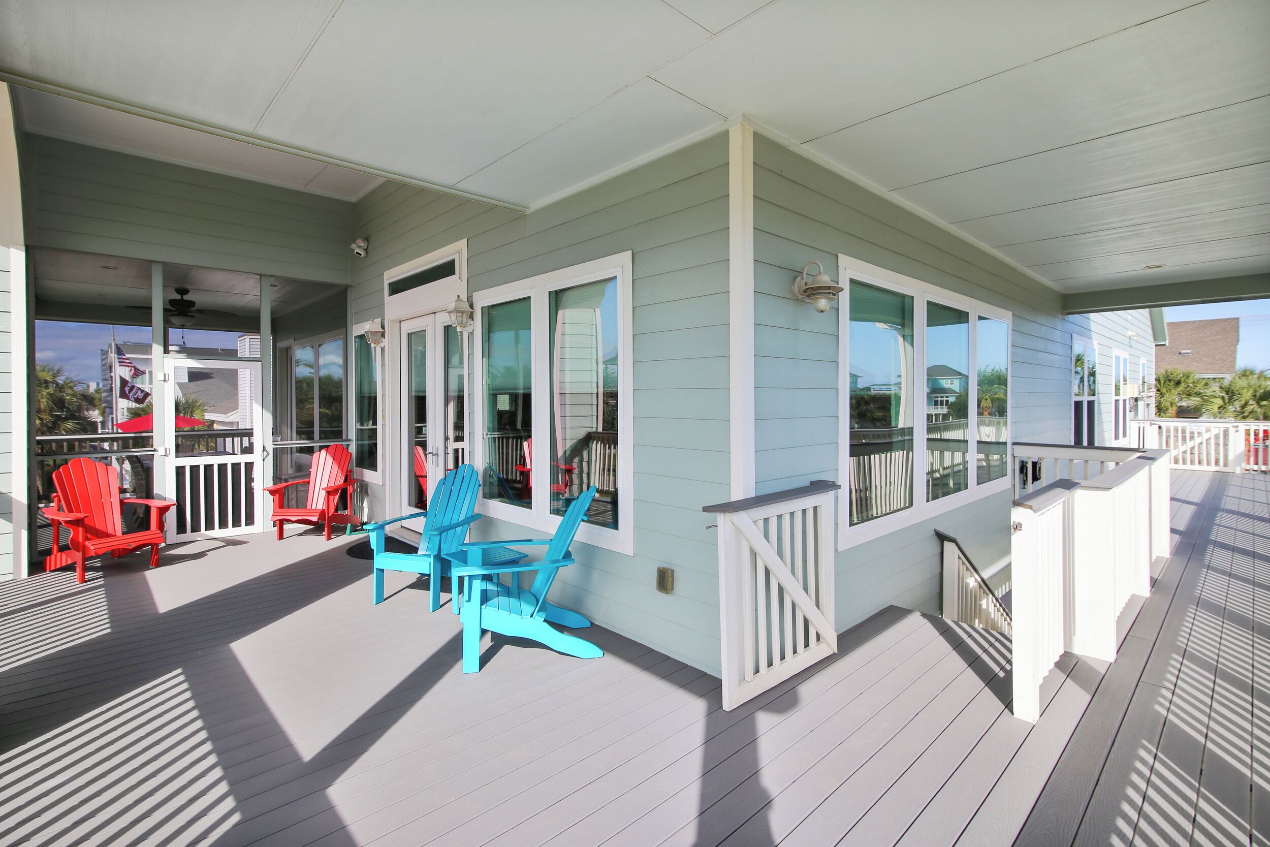 A covered porch with red and blue Adirondack chairs, a table, and a white railing.