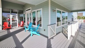 A covered porch with red and blue Adirondack chairs, a table, and a white railing. - Sandpiper Treasure by Ryson Vacation Rentals (Galveston)