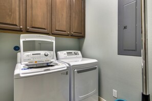 A laundry area with a front-loading washer and dryer, wooden cabinets above, and a door on the right. - Sandpiper Treasure by Ryson Vacation Rentals (Galveston)