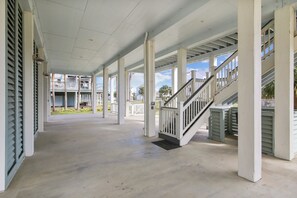 A covered outdoor area with a staircase, columns, and a view of buildings in the background. - Sandpiper Treasure by Ryson Vacation Rentals (Galveston)