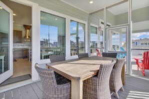 A covered outdoor dining area with a wooden table and wicker chairs, large windows, and a view of the city.