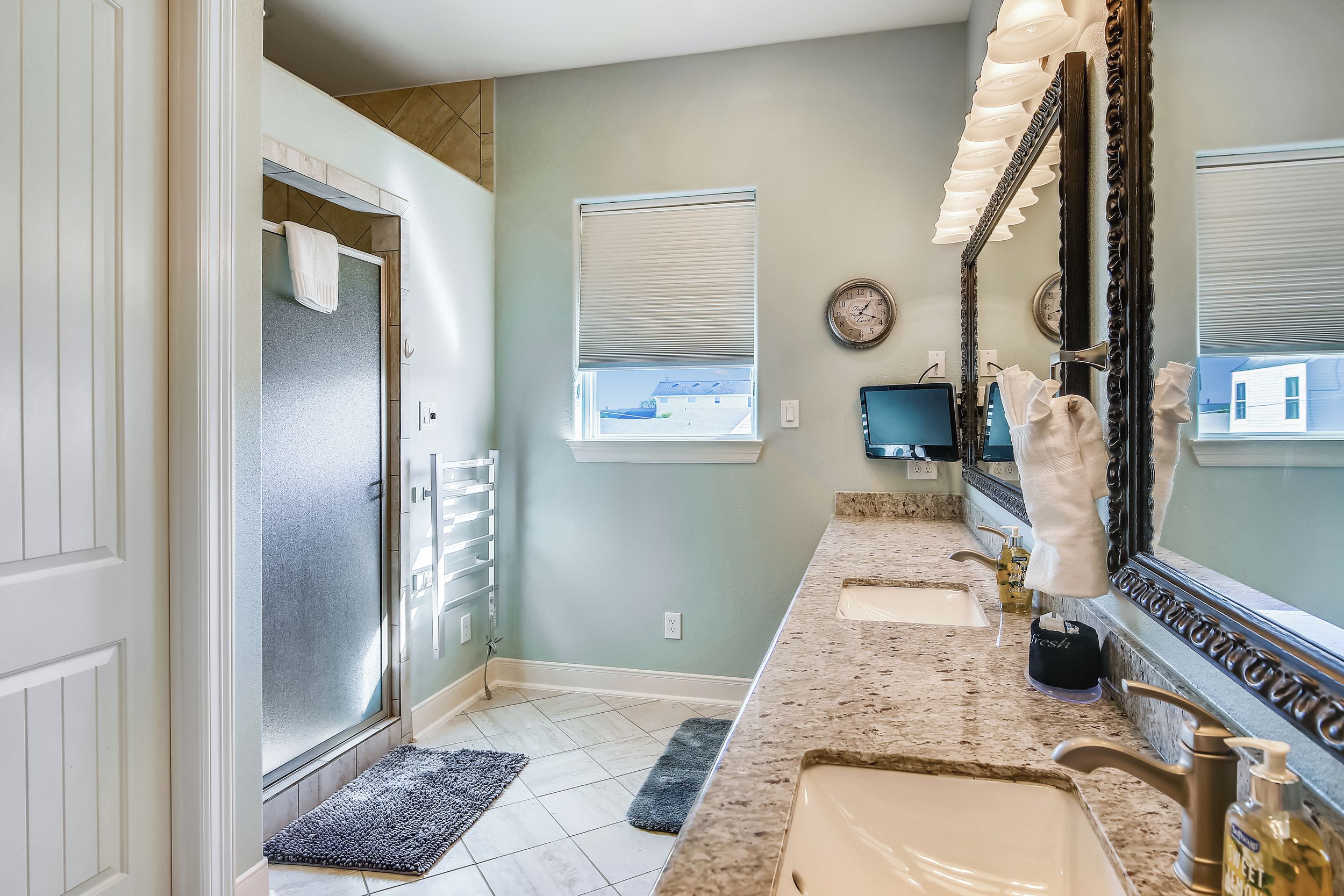 Une salle de bain avec un grand miroir, deux lavabos et une fenêtre avec des stores.