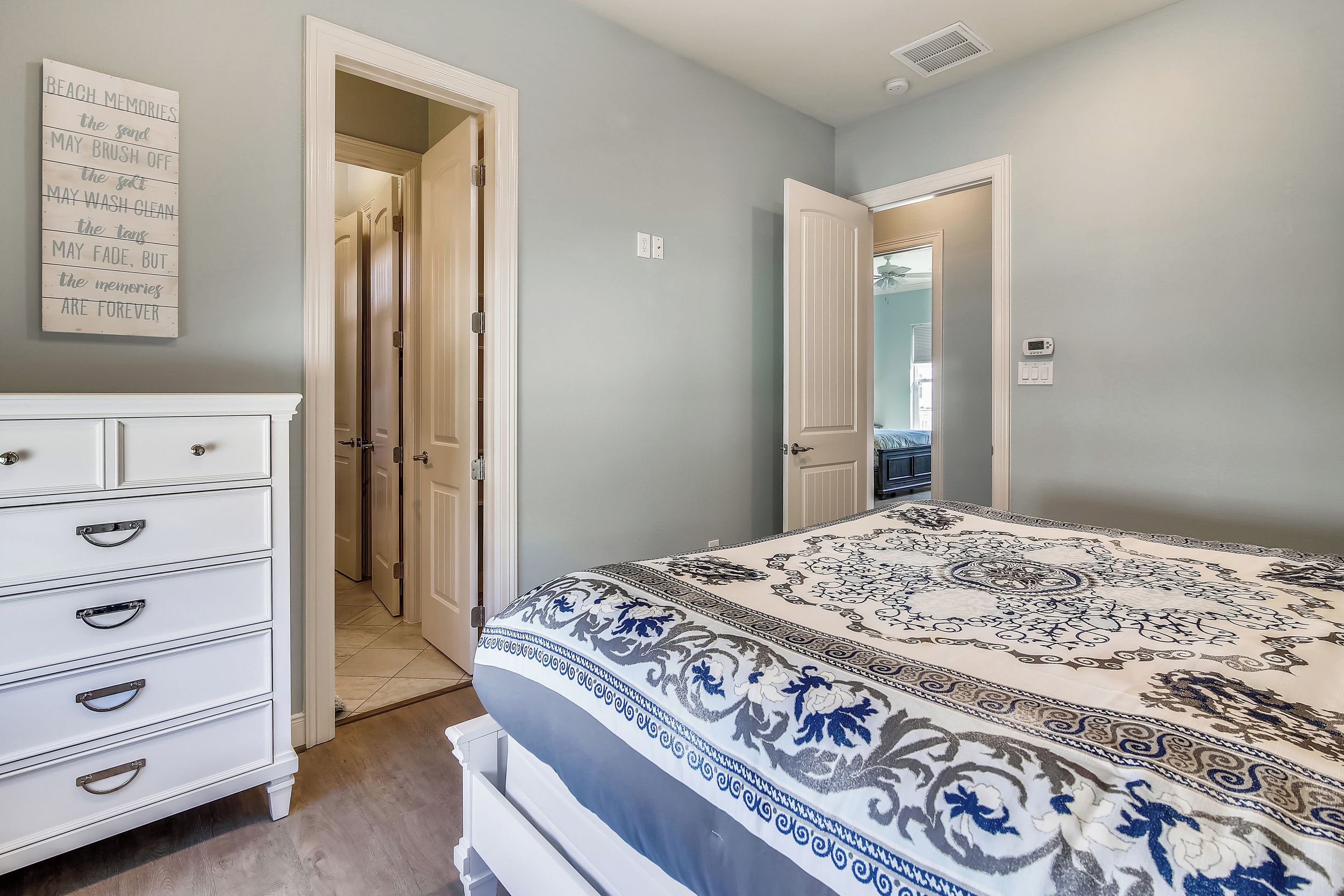 A bedroom with a bed, a dresser, and a wall with a quote. There are two doors leading to other rooms.