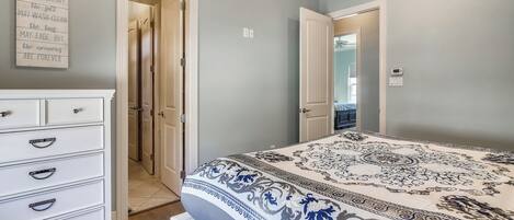 A bedroom with a bed, a dresser, and a wall with a quote. There are two doors leading to other rooms.