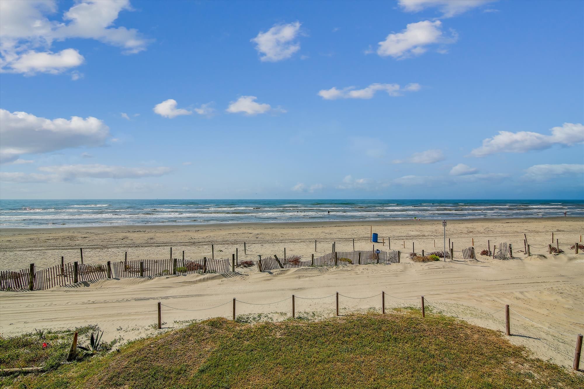 Una playa con una valla de madera y una zona verde al frente.