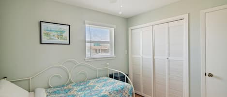 Ein Schlafzimmer mit Bett, Deckenventilator, Fenster mit Jalousien, einer Tür mit Schrank und einem gerahmten Bild an der Wand.
