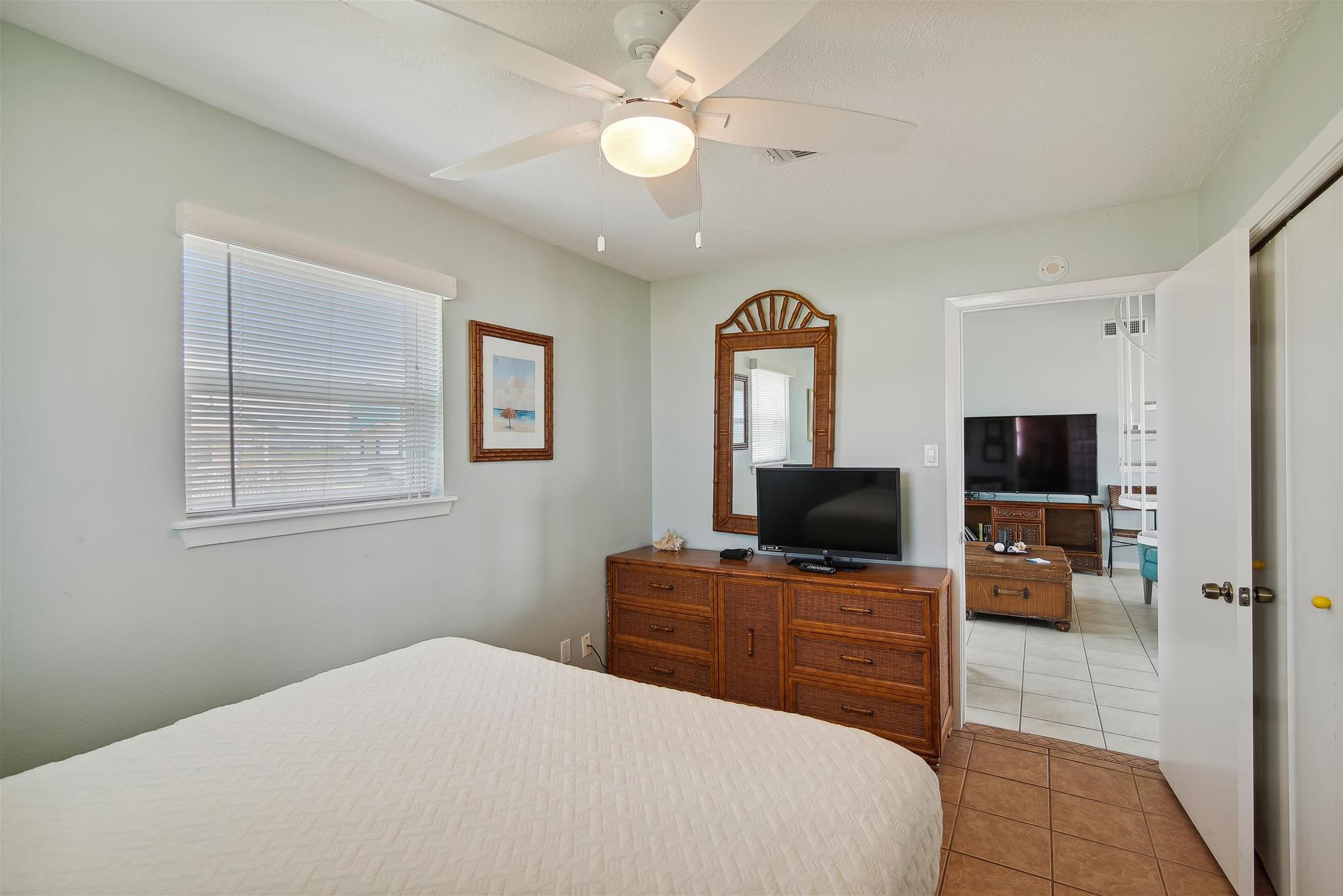 A bedroom with a bed, a dresser, a television, and a ceiling fan.