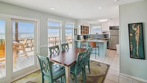 A spacious kitchen with a large island, a dining area with a wooden table and chairs, and a view of the beach through large windows. - Sea Loft by Ryson Vacation Rentals (Galveston)